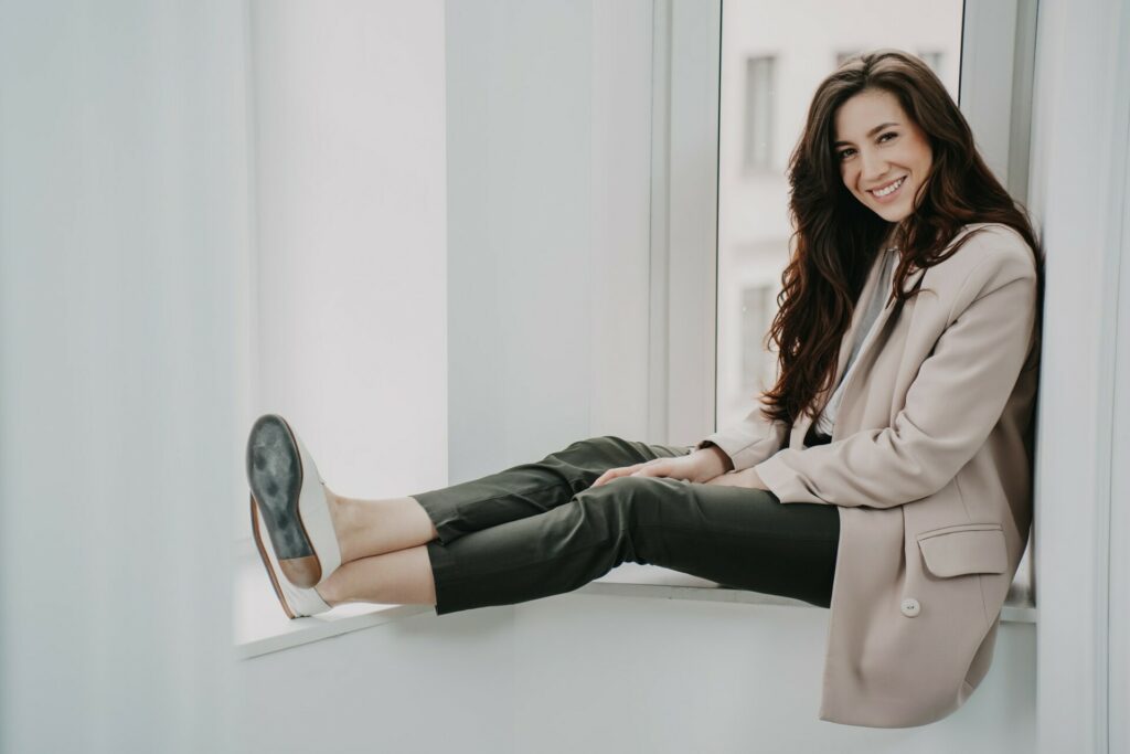 Elegant brunette woman in jacket sits on chair at mirror looks at camera. Confidence women, fashion